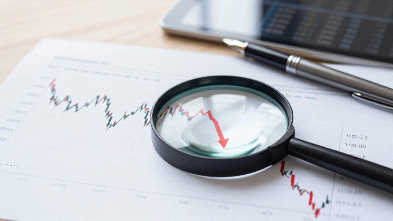 Una lupa sobre un gráfico financiero se enfoca en una línea roja descendente que simboliza la volatilidad y los riesgos de la inversión.